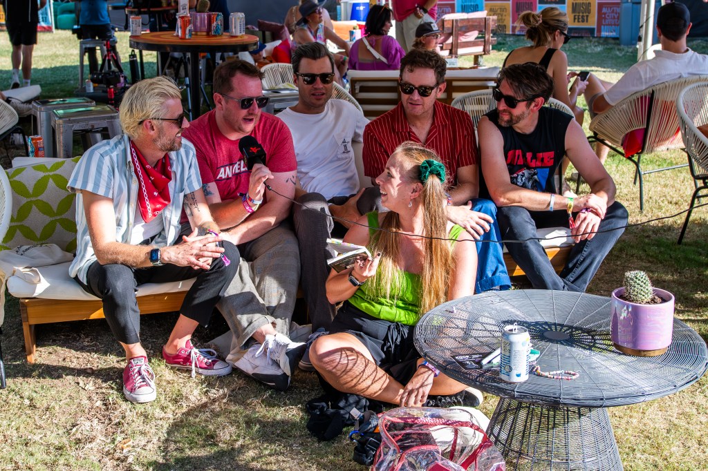 Stefny sits in front of Something Corporate holding a book and looking back at Josh while Josh holds the mic.